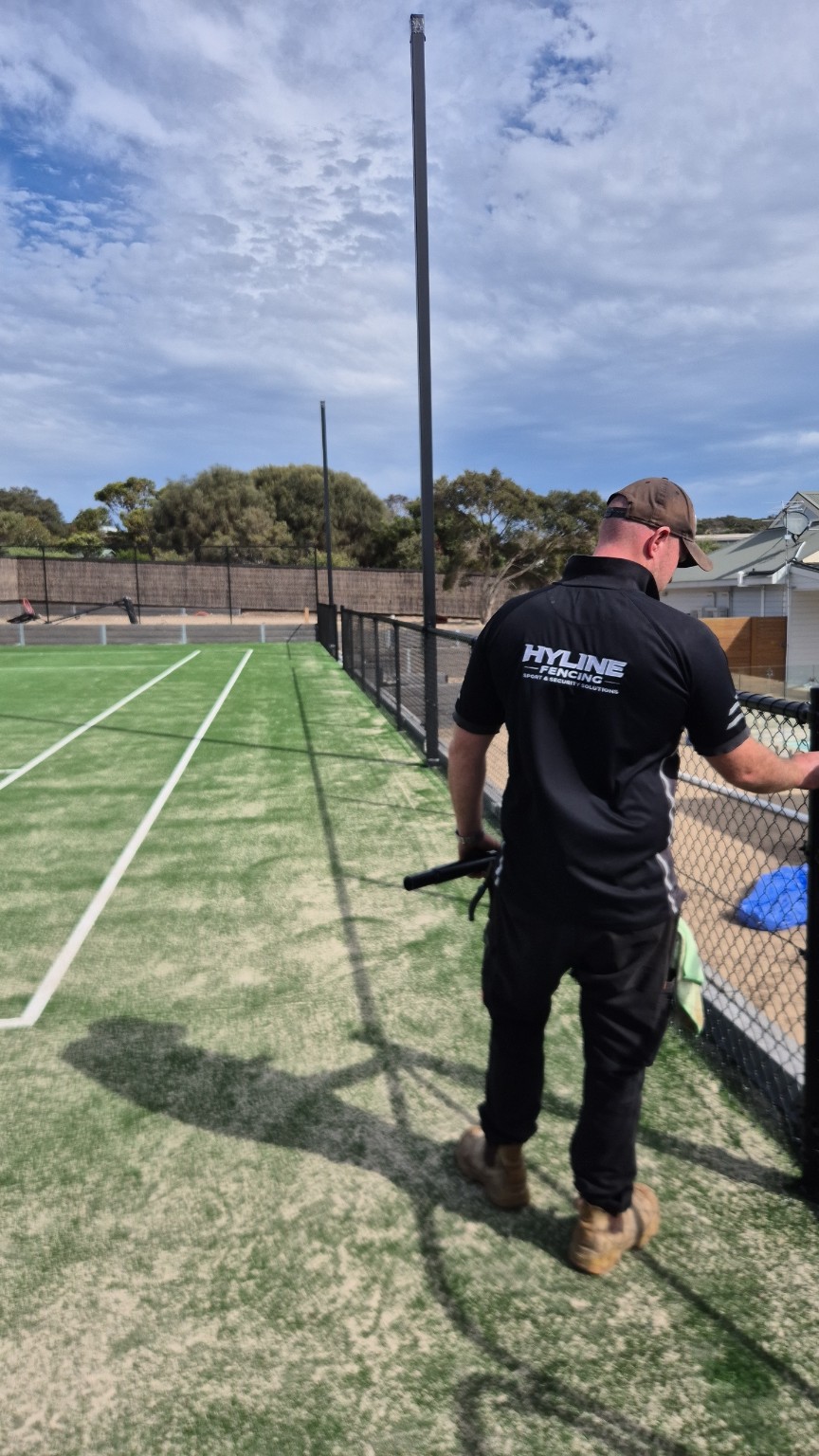 Hyline team member beside the black chain mesh side fence at the Blairgowrie backyard tennis court