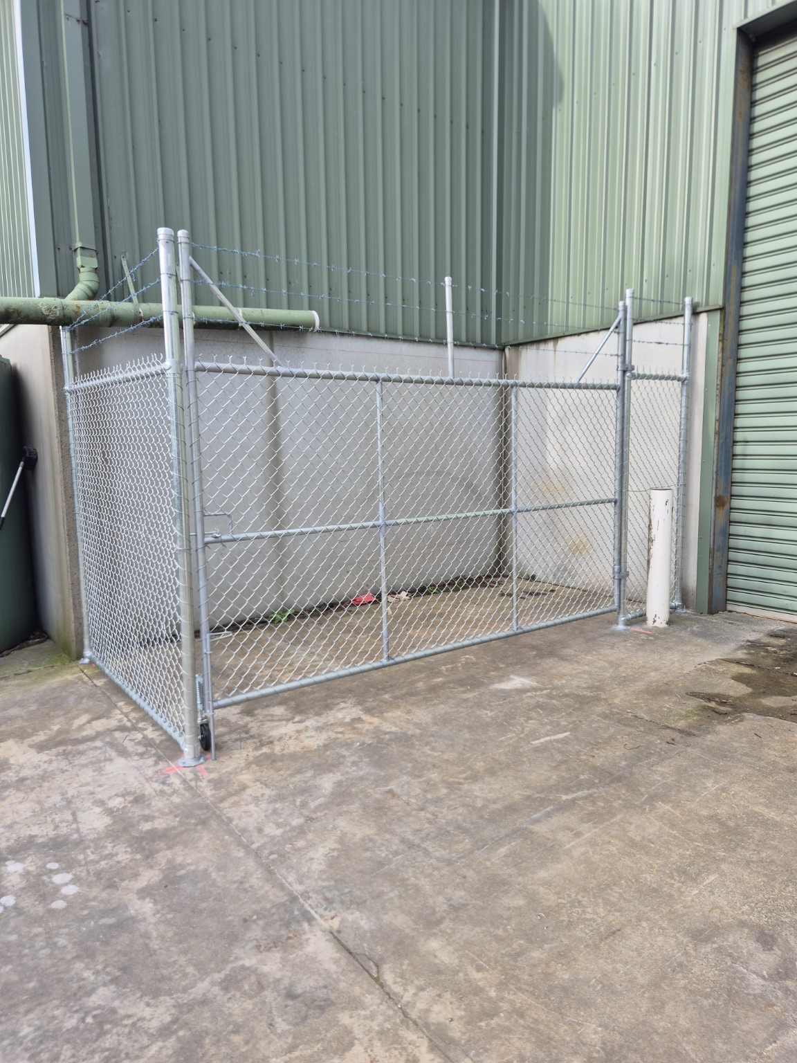 Large galvanised swing gate with a support wheel at the base of the gate in a Burra Sheetmetal security enclosure