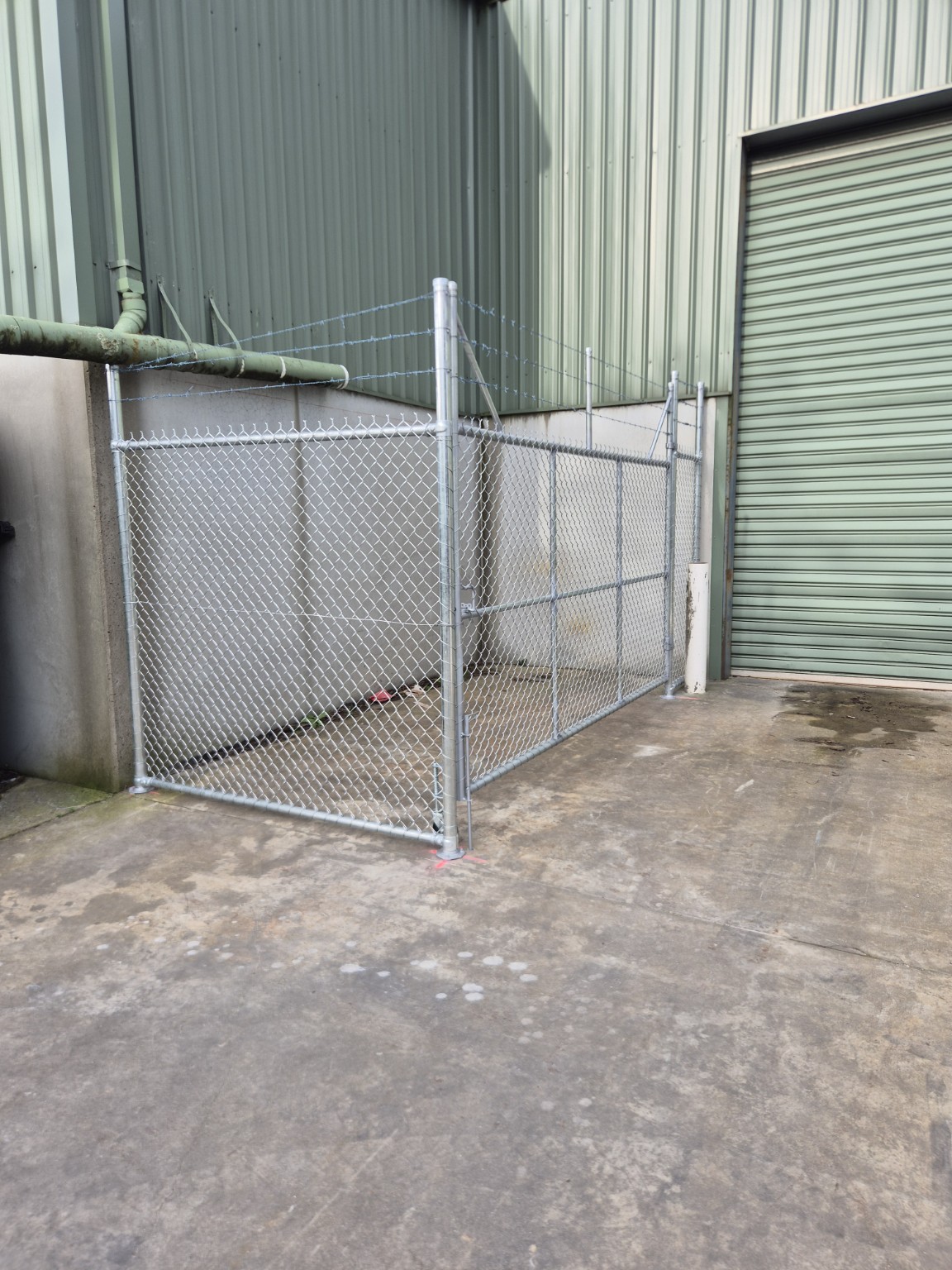 Corner view of a galvanised chain mesh enclosure showing top and bottom rails and base-plated posts