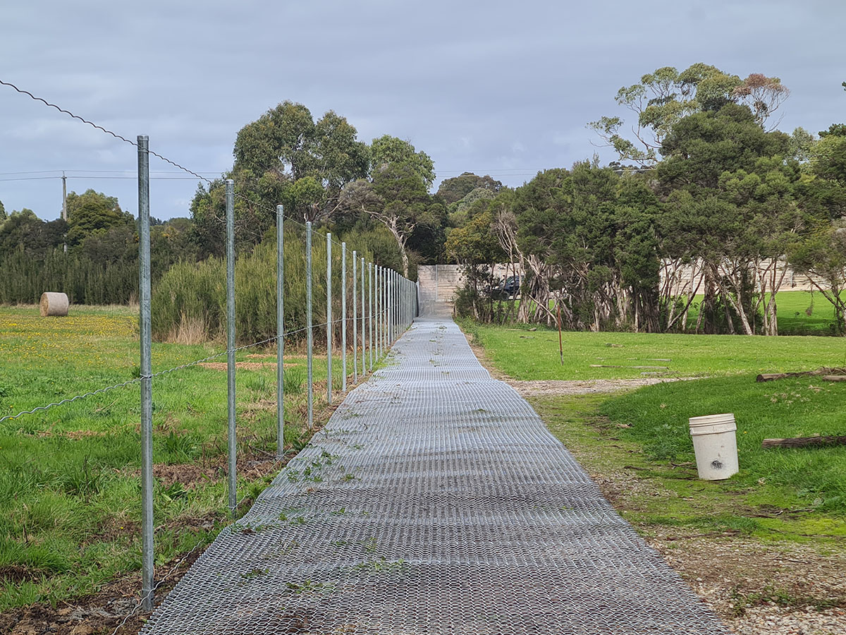 Galvanised chain mesh fencing installation in progress along a rural track