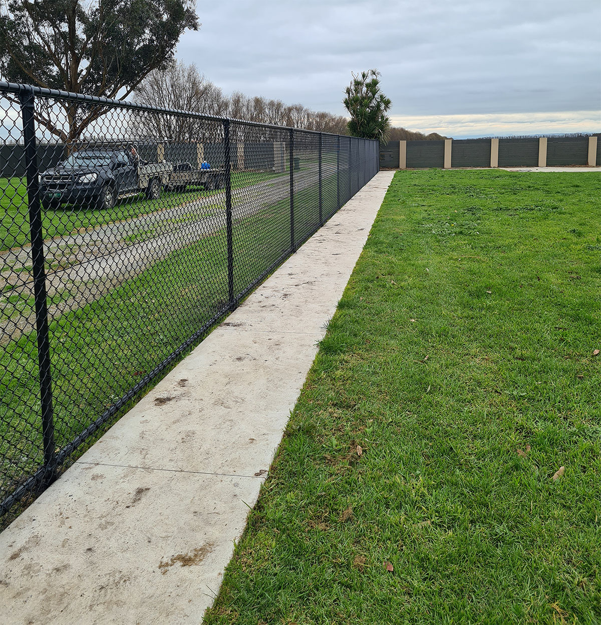 Black chain mesh boundary fencing beside a concrete path and lawn
