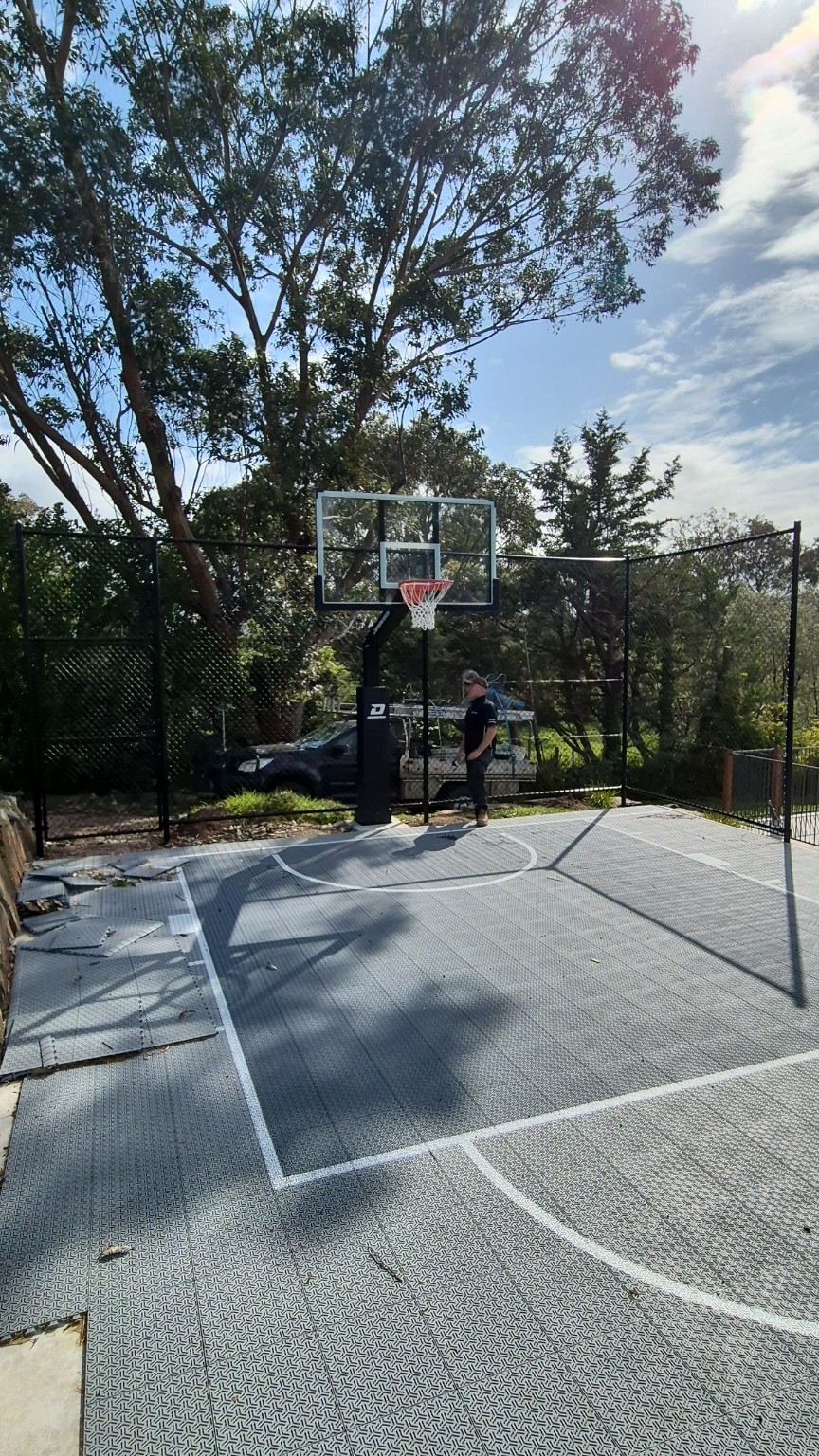 Black chain wire fencing with top and bottom rails behind the backyard basketball hoop