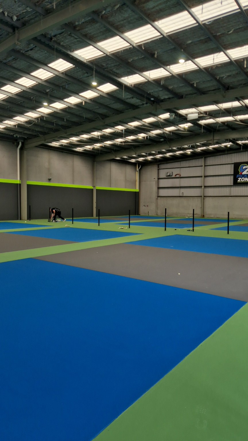 Hyline installing base-plated posts on the surfaced indoor pickleball courts at Pickle Zone