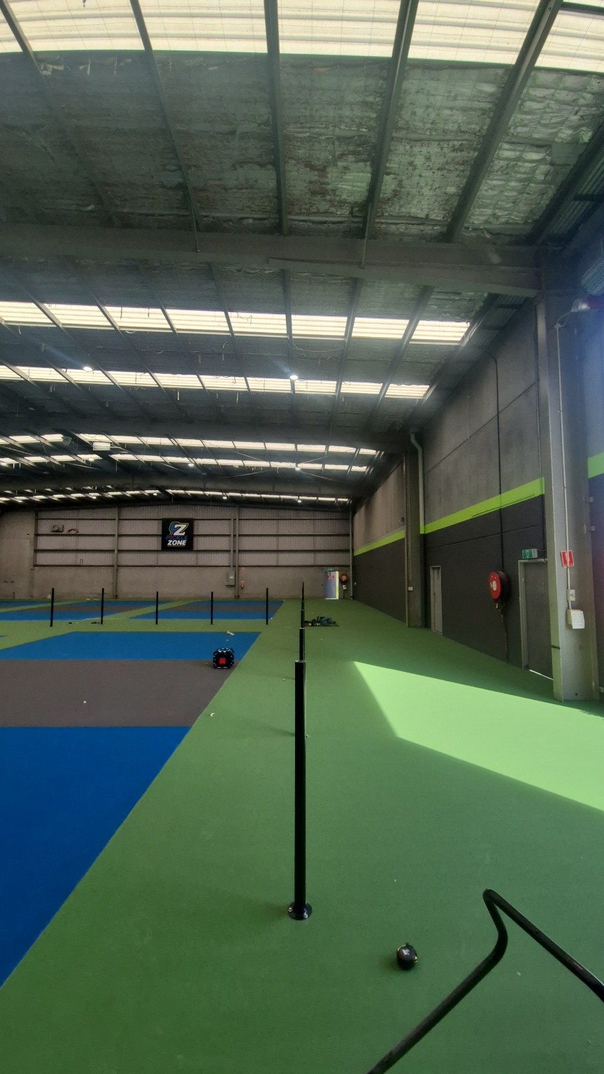 Black bolt-down posts installed along the court walkway before fitting rails and mesh