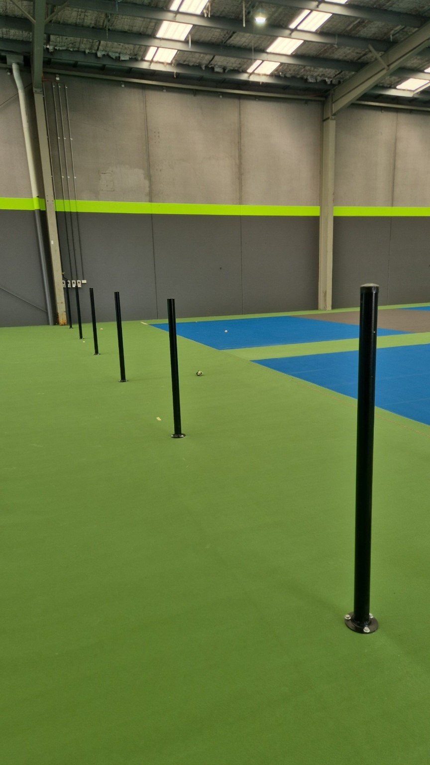Black powder-coated posts fixed to the indoor court surface before mesh installation