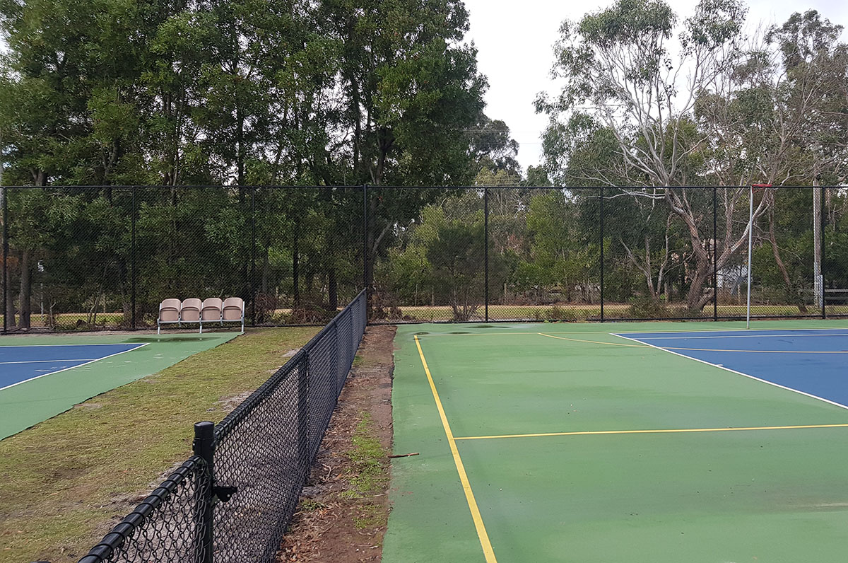 Long black chain mesh fencing alongside red clay tennis courts under court lighting