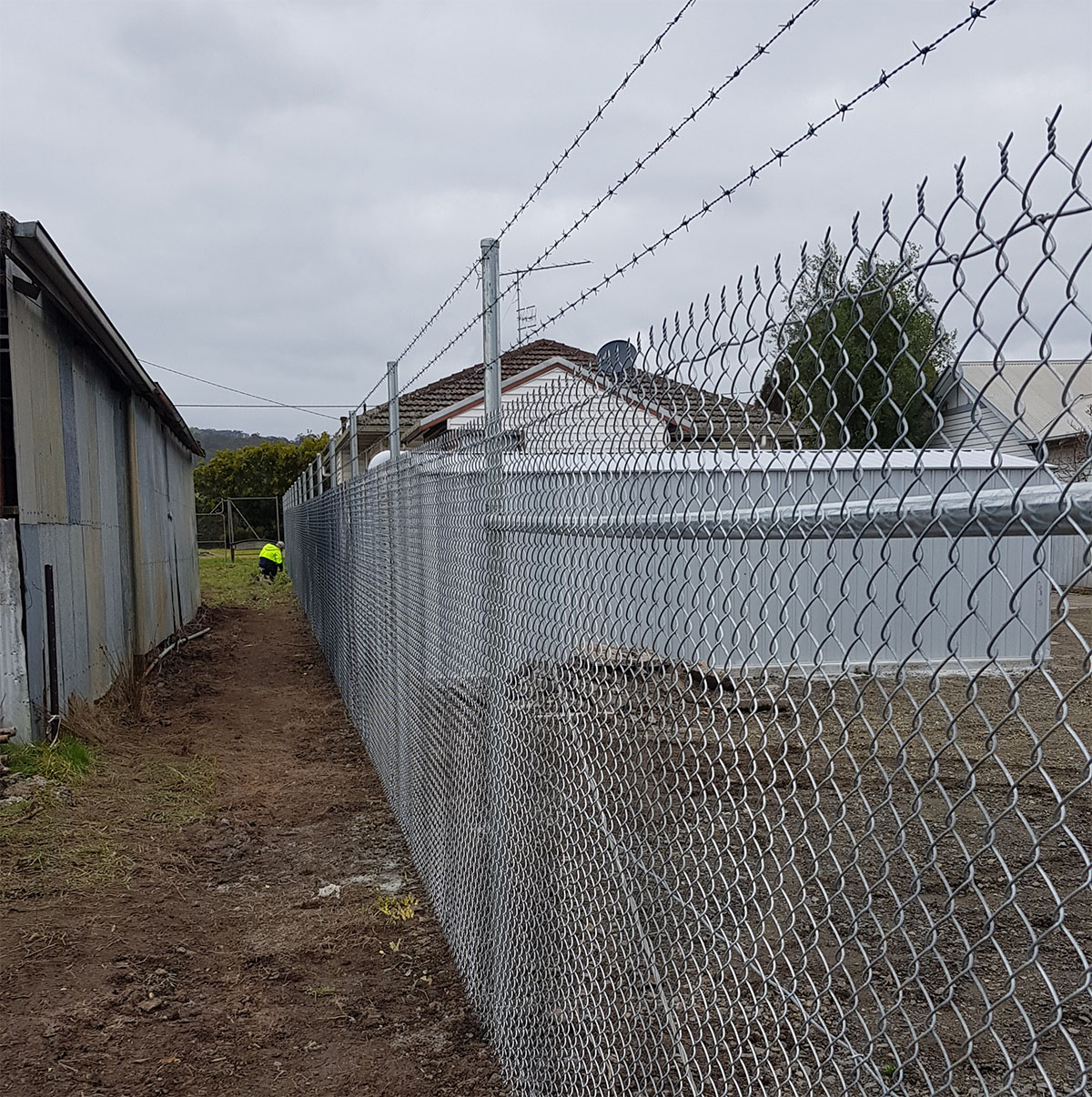 Galvanised chain mesh security fencing with top wires and access gate on a commercial site