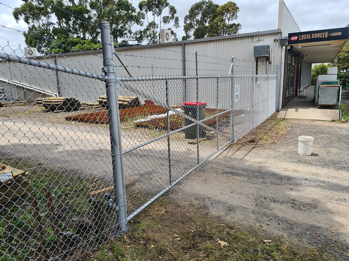 Long galvanised chain mesh security fence with barb wire topping beside an industrial boundary