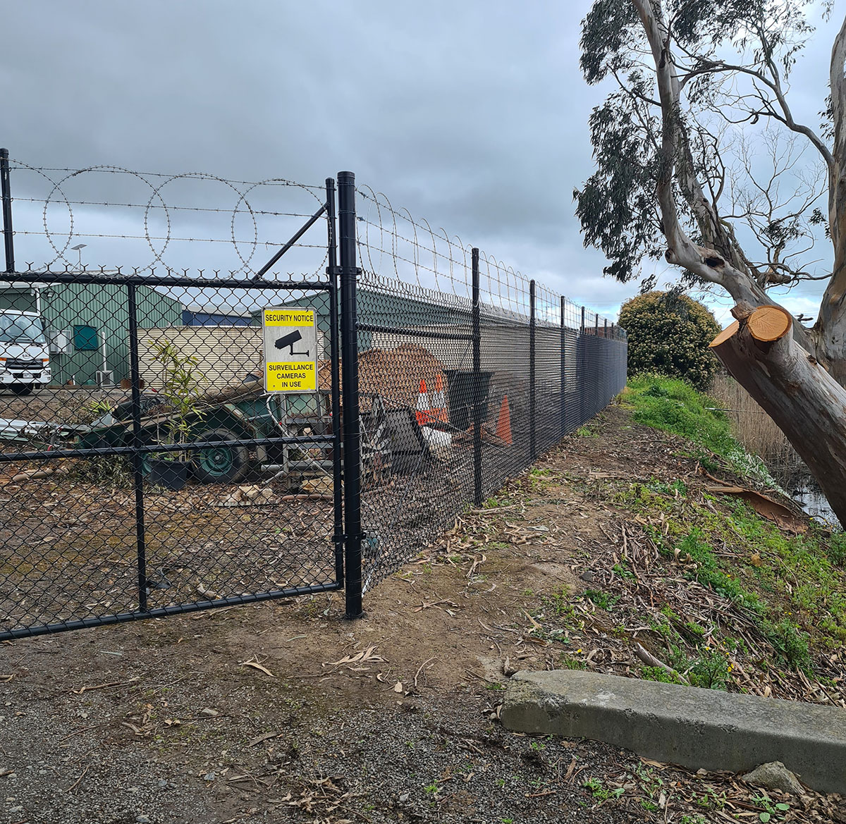 Long black chain mesh security fence with protective topping wire along a commercial boundary