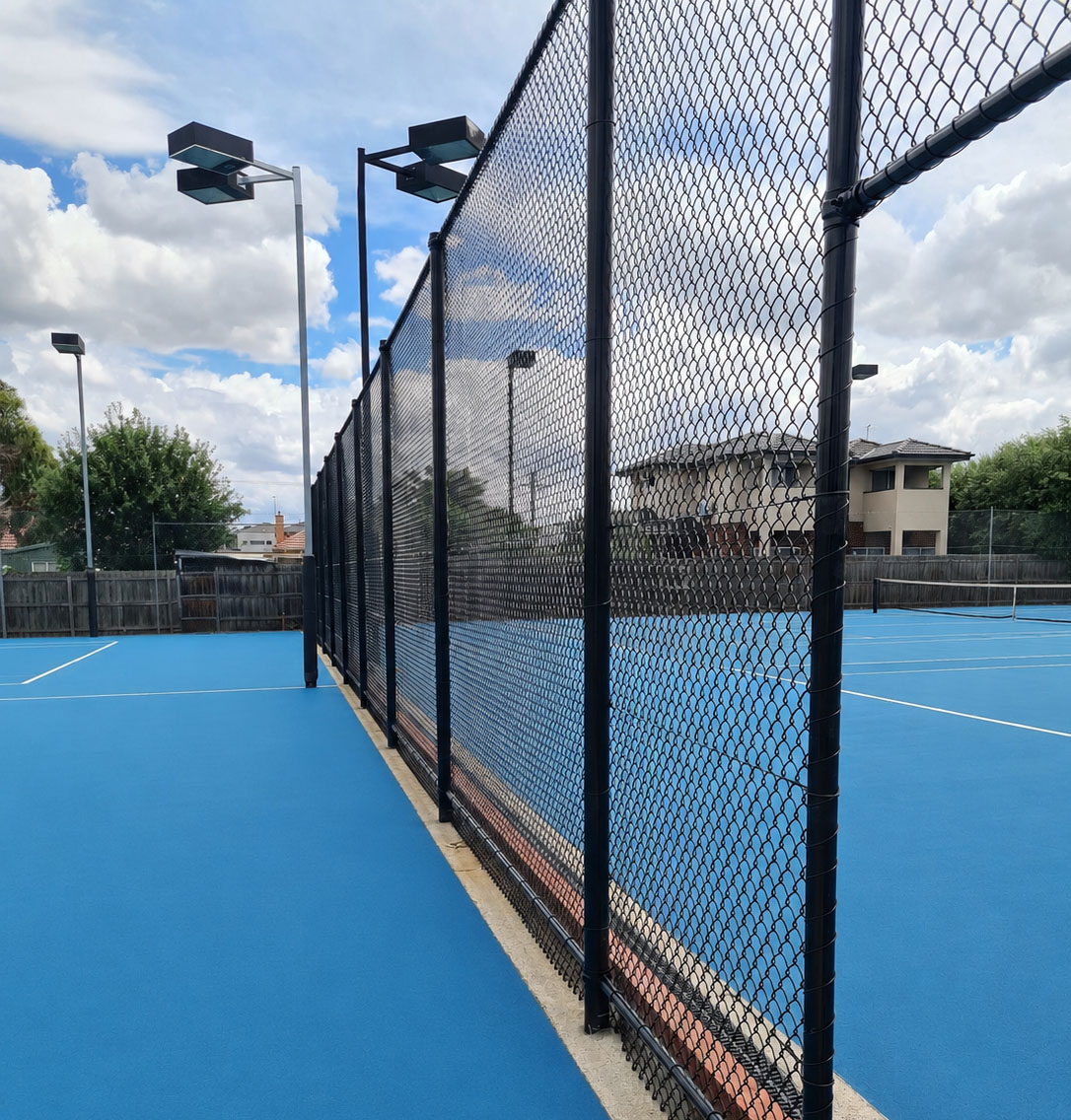Renewed blue tennis court surface with black chain mesh fencing