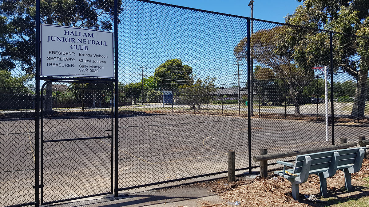 Outdoor synthetic sports court with black chain mesh fencing and landscaped pathway