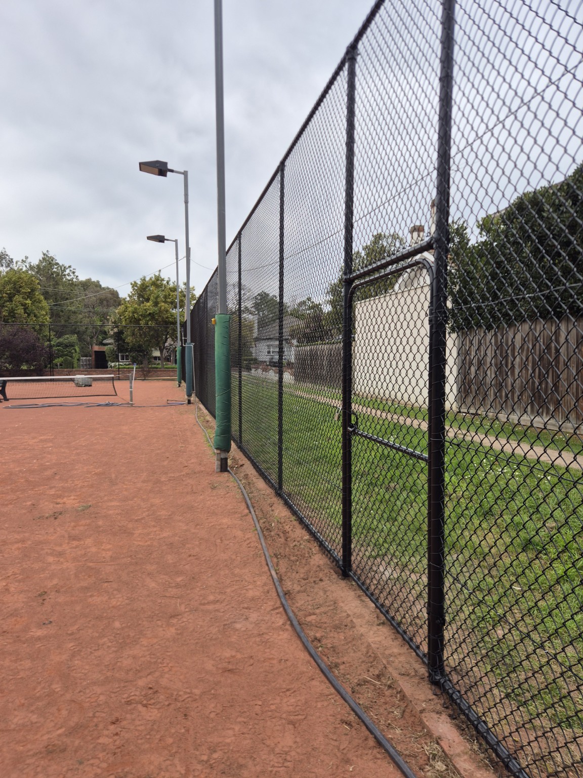 Completed black PVC-coated chain mesh tennis court fence and pedestrian gate at Willison Park Tennis Club in Camberwell