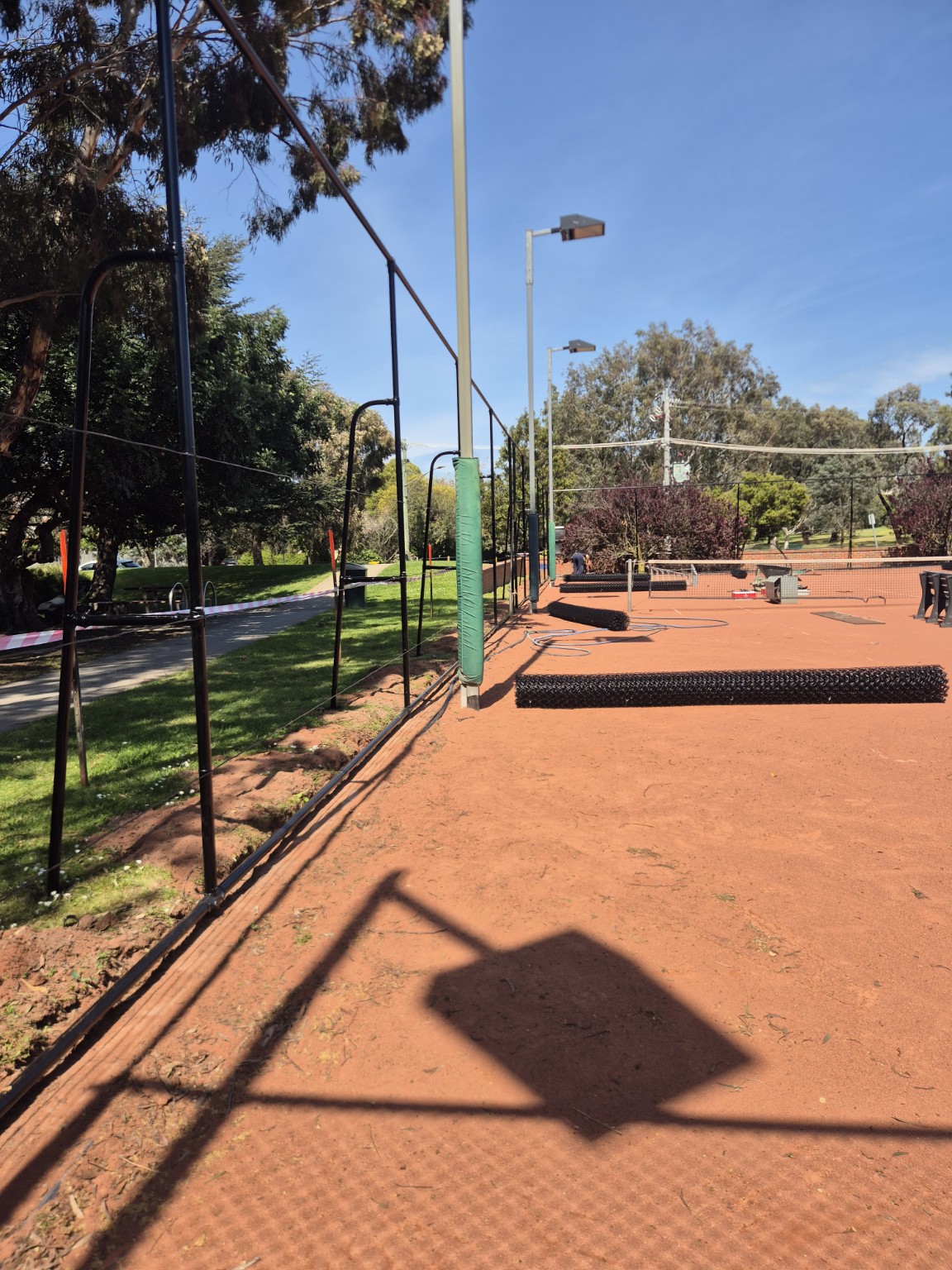 Black framework and gate opening with new chain mesh rolls laid out beside the tennis courts